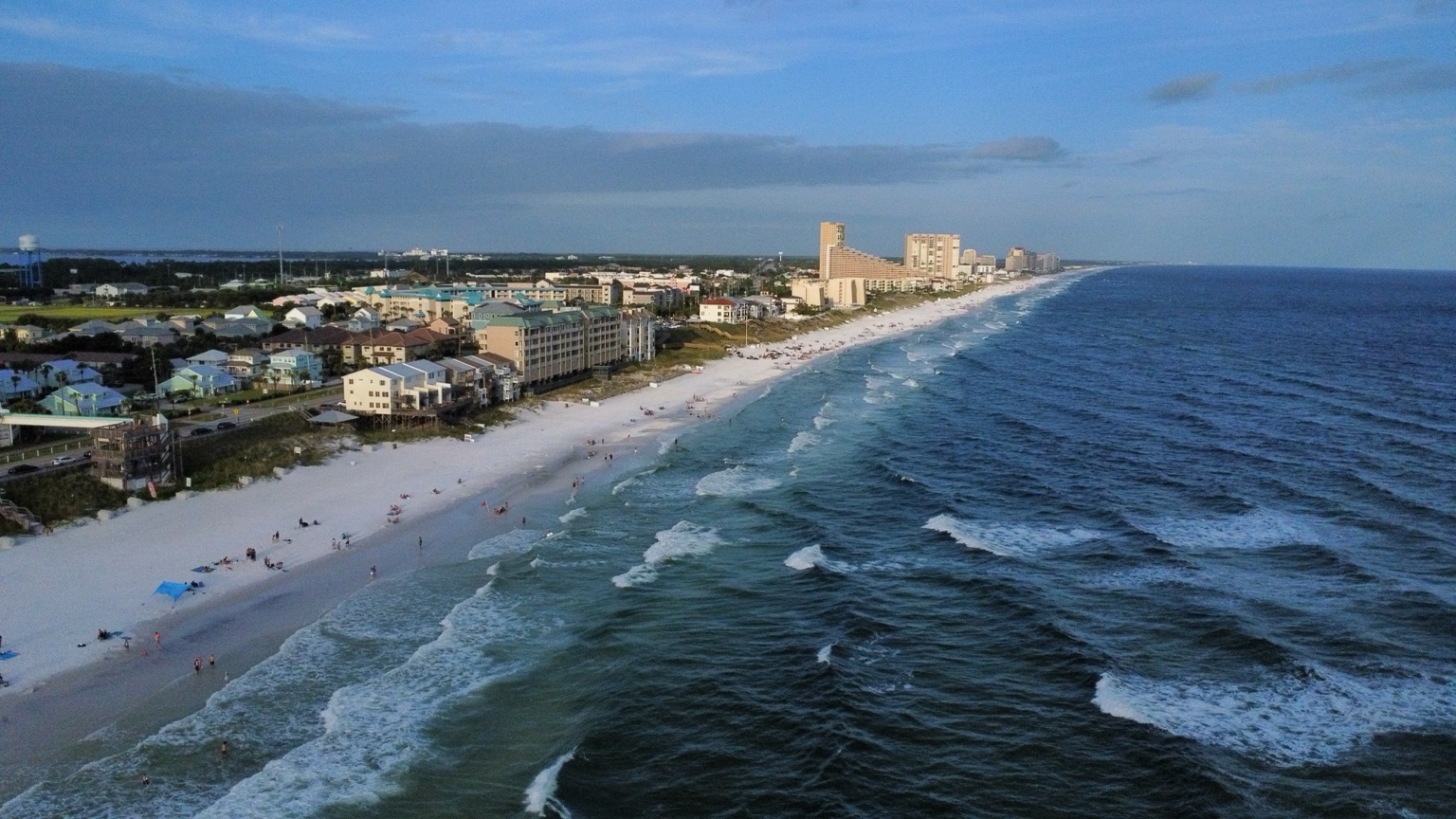 Aerial coastal photograph showing a beach, shoreline, and surrounding community